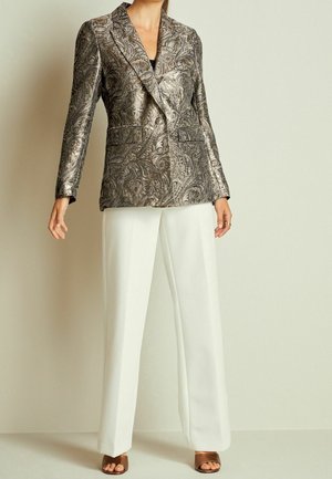 Blazer à motifs métalliques en argent et noir, avec un design à double boutonnage et deux poches avant, associé à un pantalon large blanc.