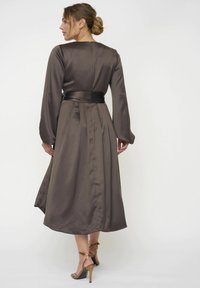 Braunes Satin-Kleid mit langen Ärmeln, einem Taillengürtel und einem ausgestellten Rock. Verfügt über einen hohen Ausschnitt und eine glatte, glänzende Textur.