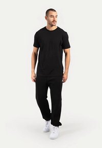 Schwarzes Baumwoll-T-Shirt und passende Jogginghosen, beide mit schlichtem Design. Weiße Turnschuhe runden das Outfit ab. Keine Muster oder Akzente vorhanden.