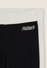 Sezione di abbigliamento in bianco e nero con il logo "FREDDY" in testo stilizzato bianco su tessuto nero vicino alla cucitura.