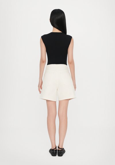 Μαύρο αμάνικο τοπ σε συνδυασμό με κρεμ σορτς ψηλόμεσο, με κομψή γραμμή και πίσω τσέπες, καθώς και μαύρα slip-on παπούτσια με τρουκς.
