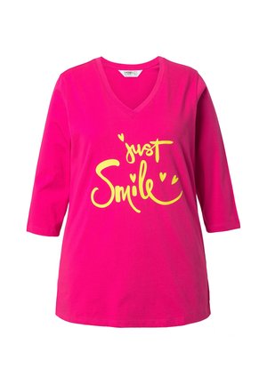 T-shirt in cotone rosa acceso con scollatura a V e maniche a tre quarti. Presenta testo giallo con scritto "just Smile" e decorazioni a forma di cuore.