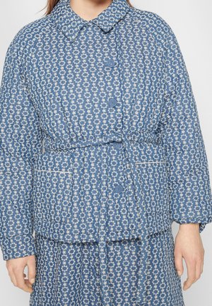 Veste matelassée bleue avec motif floral blanc, boutonnée devant, ceinture assortie et grandes poches avant portée par une personne.
