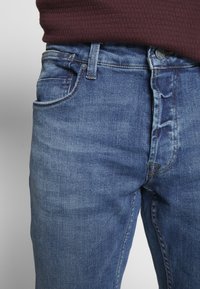 Lichtblauwe spijkerbroek met een mid-rise taille, voorzien van vijf zakken, subtiele vervaging en contrasterende stiksels voor extra detail.