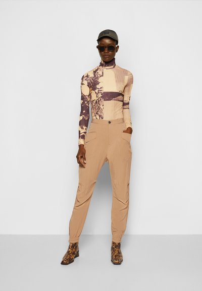 Camisola de manga longa em bege com um padrão floral roxo, combinada com calças largas castanhas claras e botins com padrão de animal.