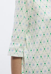 Κοντομάνικη μπλούζα, λευκό ύφασμα με σχέδιο πράσινες και ανοιχτό μπλε καρδιές, με απαλή υφή και λεπτομέρεια ρεβέρ.