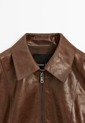 Veste en cuir marron avec un col pointu, fermeture éclair à l'avant et finition texturée. Étiquette intérieure visible avec le nom de la marque.