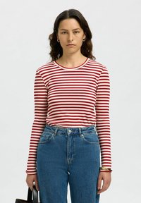 Långärmad randig tröja i röd och vit ribbad tyg, kombinerad med högmidjade blå denimjeans. Har rund hals och en tight passform.