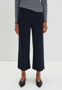 Pantaloni a gamba larga blu navy con pince, realizzati in un tessuto liscio. Abbinati a scarpe nere a punta. La parte superiore presenta un motivo geometrico in blu navy e bianco.