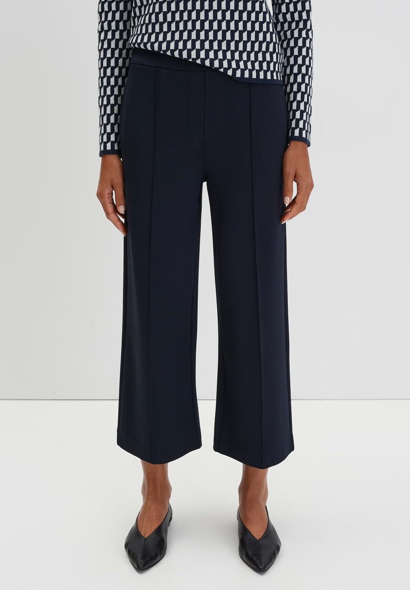 Pantaloni a gamba larga blu navy con pince, realizzati in un tessuto liscio. Abbinati a scarpe nere a punta. La parte superiore presenta un motivo geometrico in blu navy e bianco.