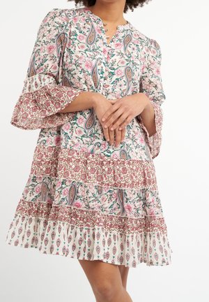 Femme portant une robe à motifs floraux et cachemire avec des manches cloche volantées et une jupe à étages, mains doucement jointes devant.
