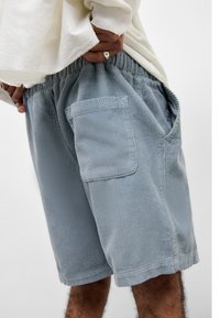 Lys blå corduroy shorts med elastisk midje og sidelommer, med subtile vertikale ribber og en liten logo detalj på lommen.