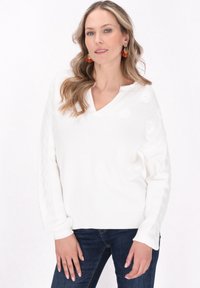 Weißer Strickpullover mit V-Ausschnitt und Zopfmuster-Details an den Ärmeln. Mit floralen Akzenten auf der Vorderseite und einer lockeren Passform.