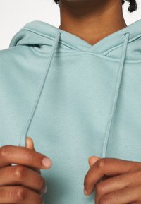 Sudadera azul claro con cordones, que presenta un corte relajado y una textura suave. Primer plano de manos sujetando los cordones.