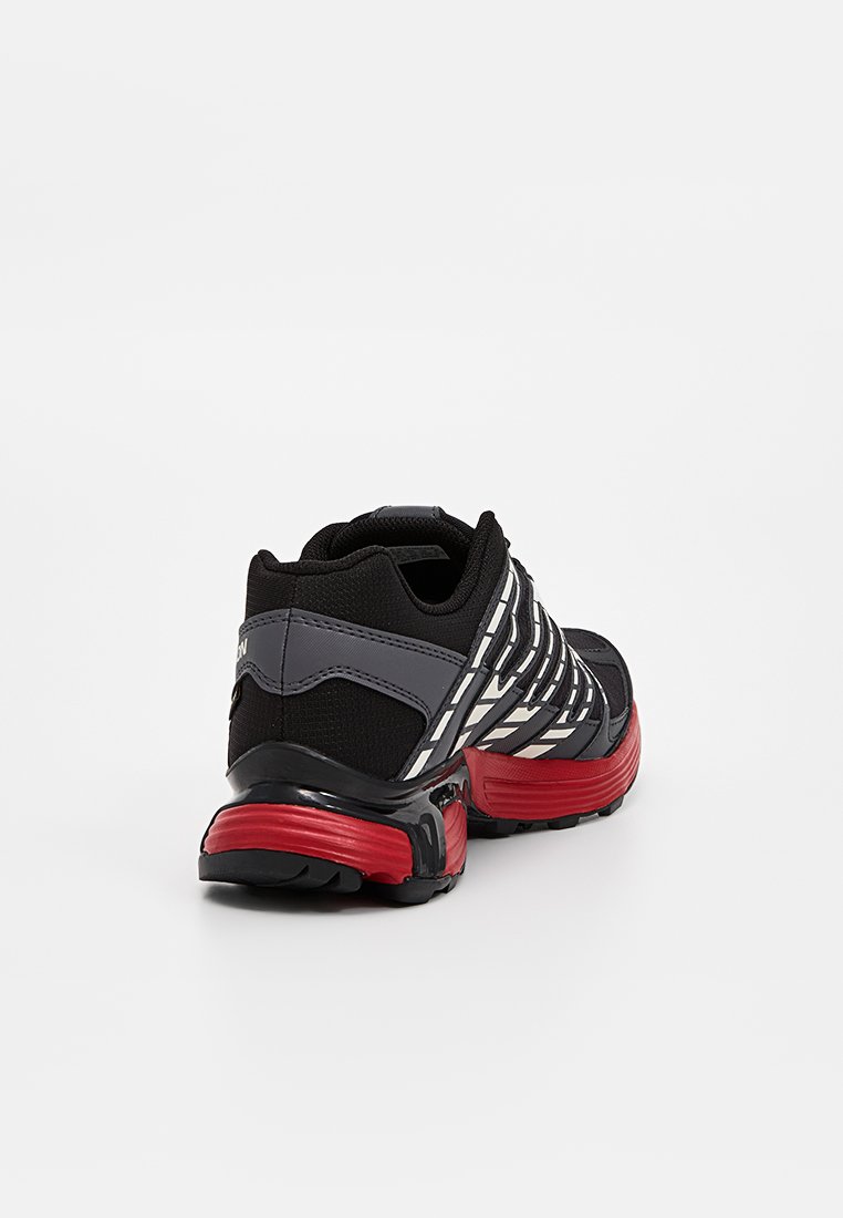 Schwarzer Sportschuh mit grauen Akzenten, ausgestattet mit einem strukturierten Obermaterial, roter Sohle und reflektierenden Streifen für bessere Sichtbarkeit. Die Rückansicht zeigt die Designdetails.