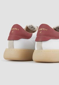 Baskets blanches avec des accents bordeaux, en cuir lisse et avec une semelle en caoutchouc. Marquage doré visible sur le contrefort du talon.