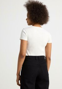 Vit ribbad topp med kort ärm och figurnära passform, tillsammans med högmidjade svarta jeans med bakfickor och en slät yta.