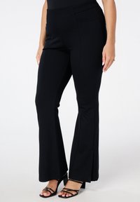 Zwarte flared broek van rekbare stof met een gladde textuur, met een strakke taille en een enkele zak op de achterkant.