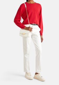 Punainen neulepaita, valkoiset housut ja kermaiset lenkkarit. Laukku on valkoinen, jossa on kullanväriset metalliosat ja ketjusanka. Asu on rento ja väljä.