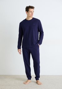 Marineblaue, gerippte Langarmbluse und passende Hose, hergestellt aus weichem Stoff. Dezentes Logo-Detail auf der Brust und der Hosentasche.