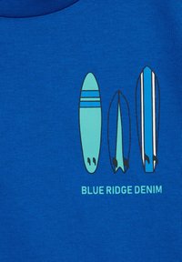 Kék póló, amelyen három szörfdeszka látható türkiz és kék színben, fekete részletekkel. Az alatta lévő szöveg: "BLUE RIDGE DENIM."