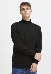Maglione a collo alto di colore nero realizzato in un tessuto morbido, con maniche lunghe e orlo a coste. Il capo presenta una texture liscia e un design minimalista.