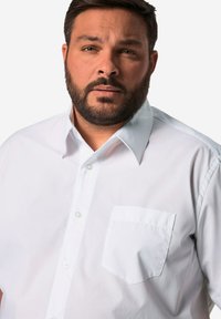 Camicia bianca con bottoni, colletto a punta, maniche corte e tasca sul petto. Presenta una texture liscia e un design classico.