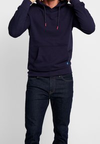 Granatowa bluza z kapturem z przednią kieszenią, kapturem ze sznurkiem i czerwonymi detalami. Nosi się z ciemnymi dżinsami. Miękki, elastyczny materiał.