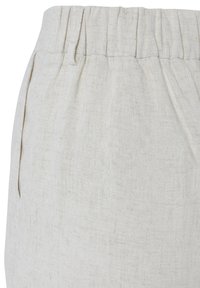 Close-up of beige linen pants waistband with elastic and front pocket on the left side.