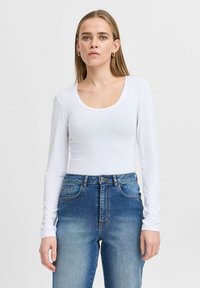 White long-sleeve bodysuit with a scoop neck, paired with high-waisted blue jeans featuring a faded design and classic five-pocket styling.
