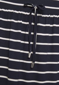 Gonna blu navy con righe orizzontali bianche, dotata di una vita elasticizzata e di un laccio di chiusura con estremità metalliche argentate. Tessuto di consistenza morbida.
