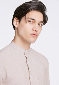 Camicia button-up beige chiaro con colletto alla coreana, tessuto testurizzato, taschino sul petto e dettagli di cucitura sottili.
