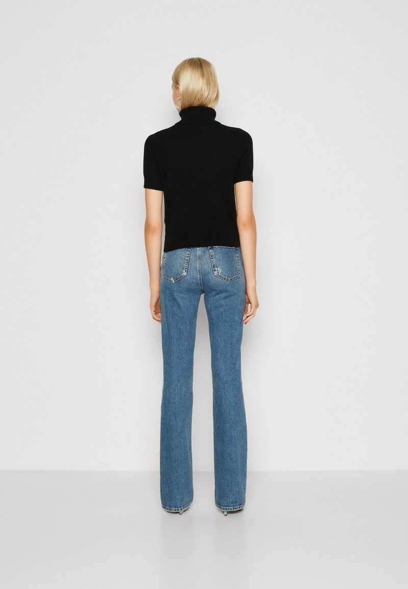 Schwarzer kurzärmeliger Rollkragenpullover, kombiniert mit hellblauen Schlagjeans. Der Pullover hat eine taillierte Passform; die Jeans verfügen über zwei Gesäßtaschen.