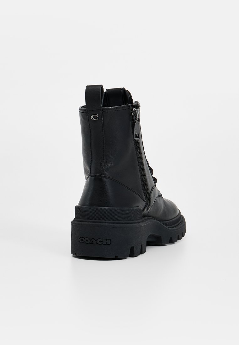 Bottine en cuir noir avec une semelle épaisse, fermeture éclair sur le côté et une petite boucle à l'arrière. Présente un logo embossé sur le talon.