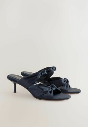 Marine satijnen muilen met een gedraaide knoopontwerp op de bovenkant, open teen en een slanke stiletto-hak. Zachte textuur en minimale hardware.