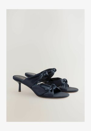 Tumesinised satiinist muulid keeratud sõlme kujundusega pealses, avatud varbaosaga ja kitsaste stiletto kontsadega. Silus tekstuur ja minimaalne riistvara.