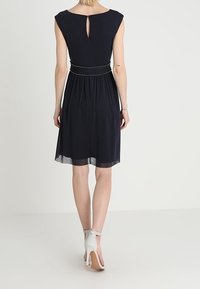 Navyblaues Kleid mit kurzen Ärmeln, einem Schlüsselloch-Rücken und einer taillierten Taille, die mit einem perlenbesetzten Gürtel geschmückt ist. Der Rock fließt mit einem leicht transparenten Saum.