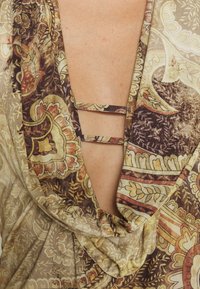 Halbtransparenter, gemusterter Stoff in erdigen Farbtönen mit floralen und geometrischen Designs. Hat einen tiefen V-Ausschnitt auf der Rückseite und zwei Stoffträger zur Unterstützung.