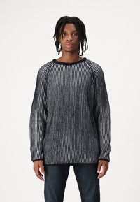 Gestreifter schwarzer und grauer Strickpullover mit rundem Halsausschnitt, Raglanärmeln und lockerer Passform. Der Stoff hat eine strukturierte Optik.