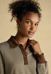 Brown houndstooth patterned polo shirt with a ribbed brown collar and cuffs, featuring buttons at the neck and a smooth texture.