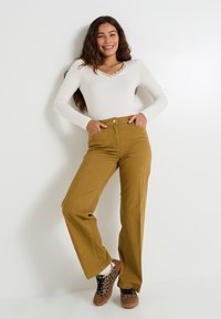 Camisa de manga larga ligera con cuello de encaje, combinada con pantalones de pierna ancha mostaza de cintura alta y zapatillas marrones con estampado de leopardo.