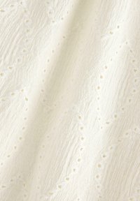 Fløjlstof med teksturerede, lodrette striber og broderede geometriske mønstre med små huller overalt.