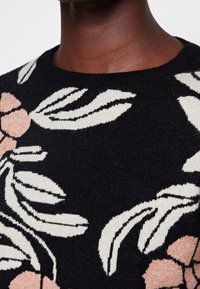 Suéter de punto con base negra y patrones florales en rosa y crema. Cuello redondo con detalle de tela texturizada.