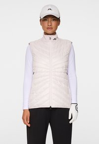 Ljusrosa, vadderad ärmlös väst med hög krage och framdragkedja, bärs över en vit långärmad skjorta, tillsammans med en keps och handskar.