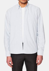 Koszula w paski, zapinana na guziki, w jasnoniebieskim i białym kolorze, wykonana z bawełny, z kołnierzykiem, długimi rękawami i prostym krojem; noszona na białym t-shircie.