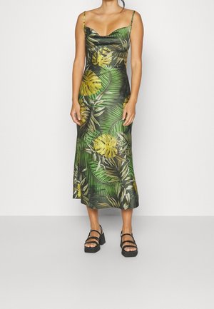 Grøn satin kjole med tropisk blad- og blomstermønster, tætsiddende liv, cowl-udskæring og ankel-længde kant. Modelen har samlet det med kraftige sorte sandaler.