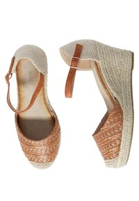 Scarpe espadrillas intrecciate di colore marrone con una cinghia alla caviglia di colore tannato e tomaia in tessuto chiaro. Presentano un tacco a cuneo rivestito di juta.
