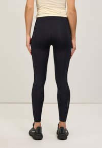 Leggings de sport noirs avec une taille haute, texture lisse et détails de couture subtils. Associés à des chaussures noires, adaptés à l'exercice.