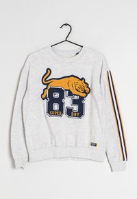 Szary sweatshirt z teksturowanym żółtym graficznym wzorem tygrysa, dużym nadrukiem "83" i napisem "SUPER DRY" poniżej; ma granatowe paski na rękawach.