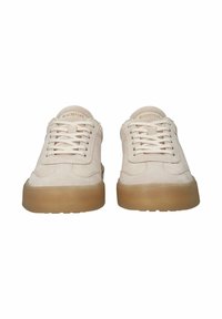 Pari beigeä mokkanahkaisia tennareita, joissa paksut ruskeat kumipohjat ja nauhat, nähtynä edestä valkoisella taustalla.